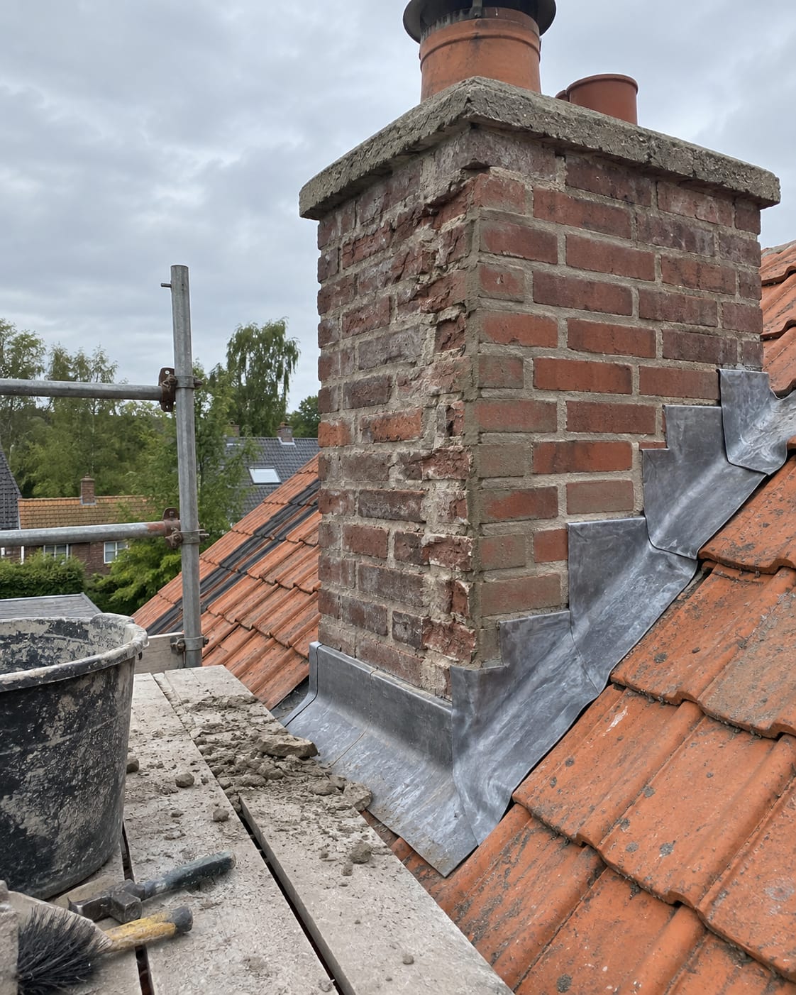 Gemetselde schoorsteen op een pannendak tijdens restauratie en herstel van het voegwerk