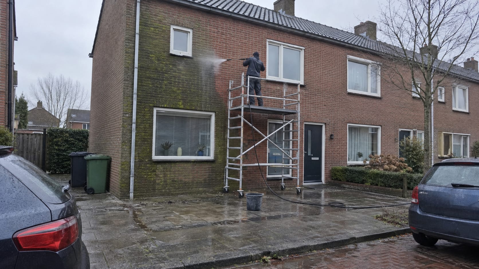 Gevelreiniger op een steiger verwijdert hardnekkige vervuiling van een bakstenen voorgevel.
